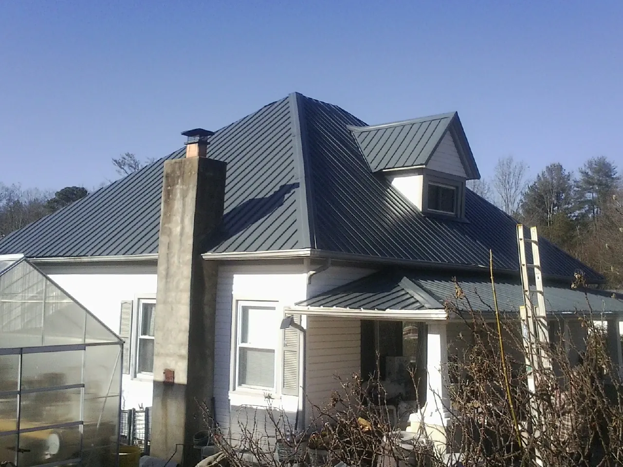 Dark blue standing seam metal roof on a white farmhouse with dormer — Slate & Tile Roof Repair by Roofing Brothers in Iuka
