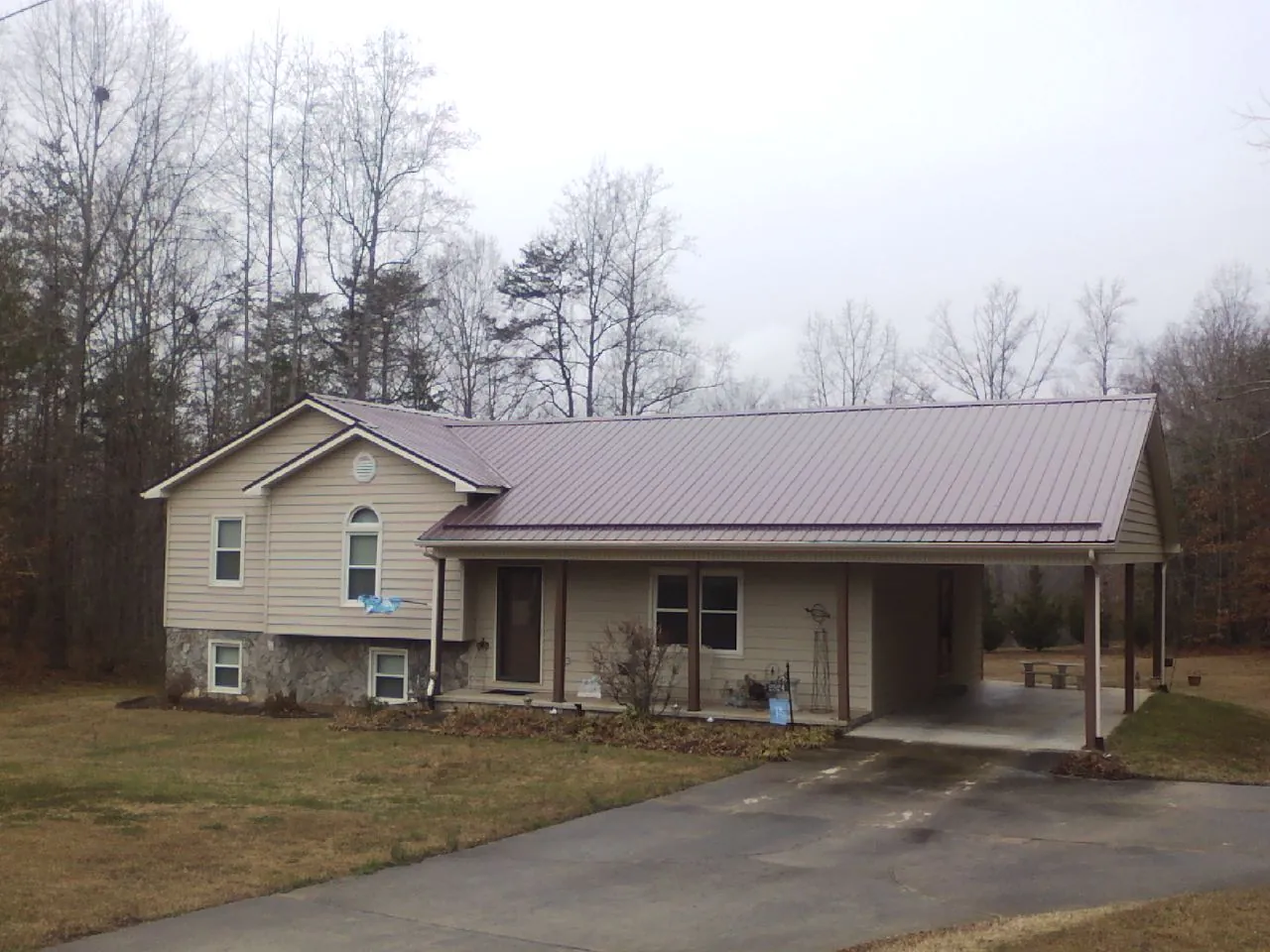 Burgundy metal roof on a tan split level home with an attached carport in Iuka