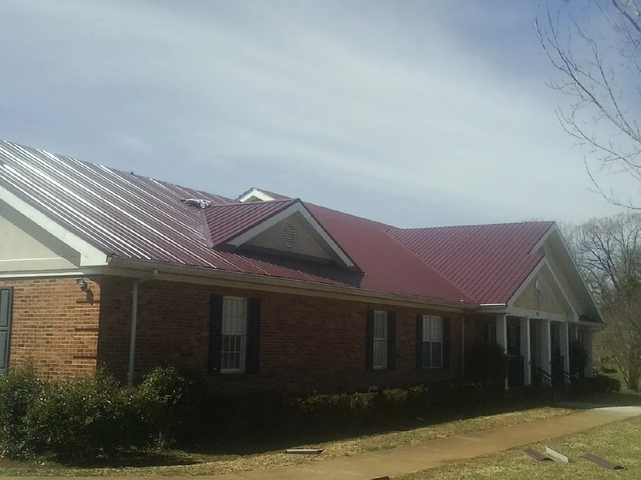 Red metal roof with gabled entries on a long brick building, from a Hail Damage Roof Repair job in Iuka