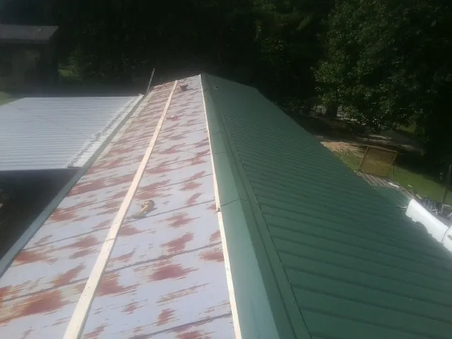 Old rusted panels beside newly installed green metal roofing — Wind Damage Roof Repair by Roofing Brothers in Iuka