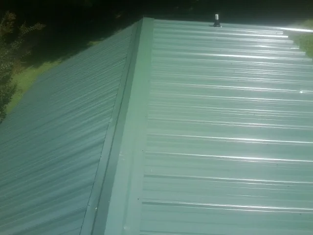 New green metal panels meeting at the ridge of a roof — Flat Roof Repair work by our crew in Iuka