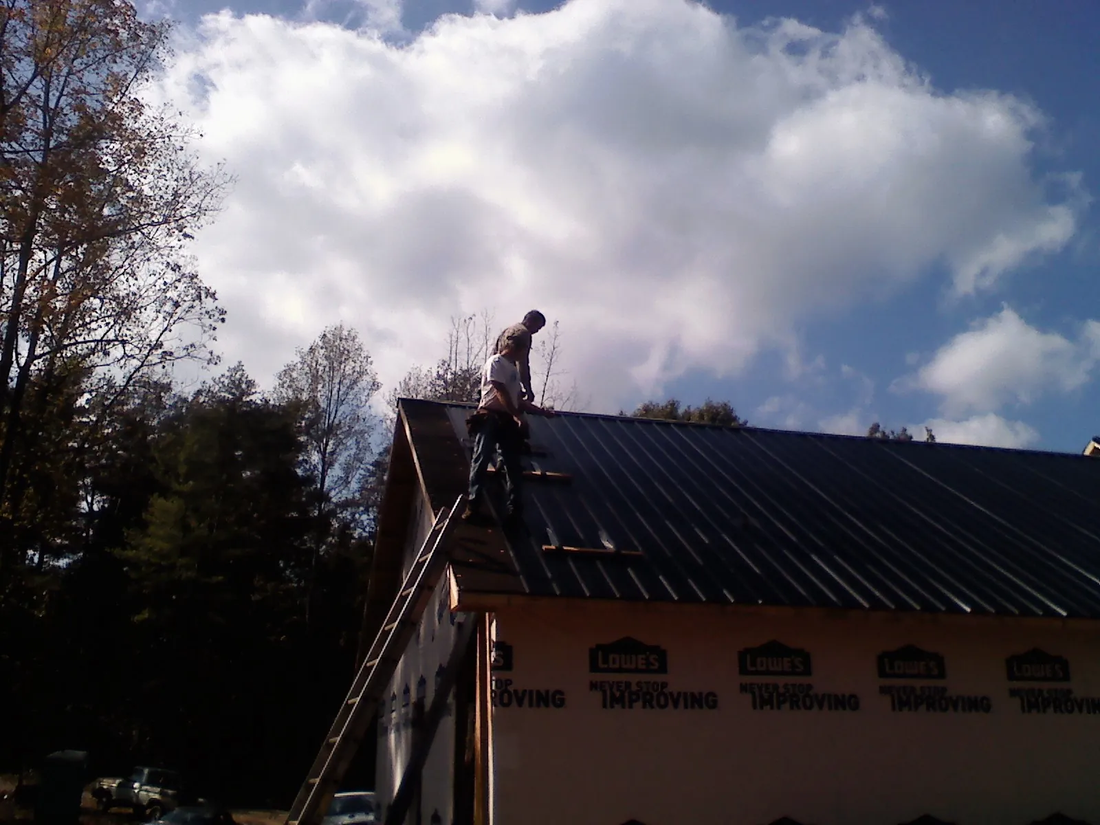 Roofer fastening dark metal panels high against a cloudy sky, from a Roof Inspection job in Iuka