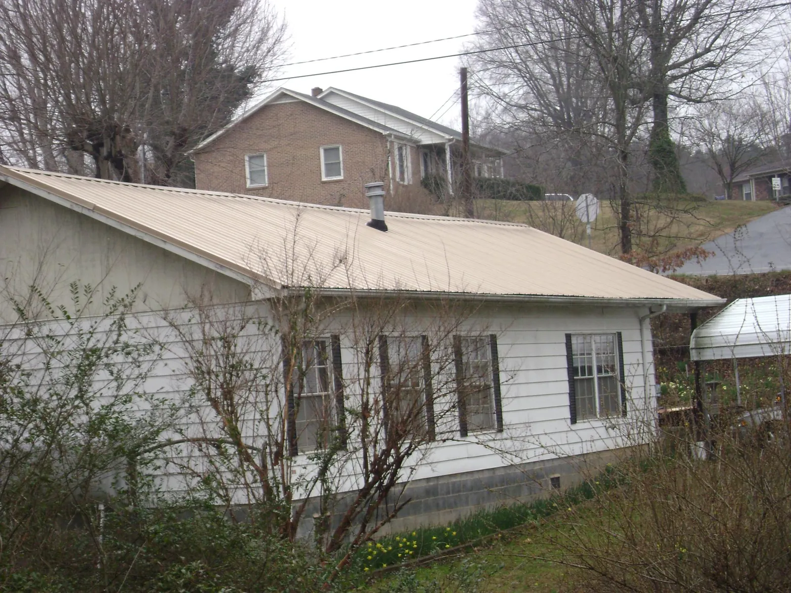 Tan metal roof on a white sided house set into a hillside — Commercial Roofing by Roofing Brothers in Iuka
