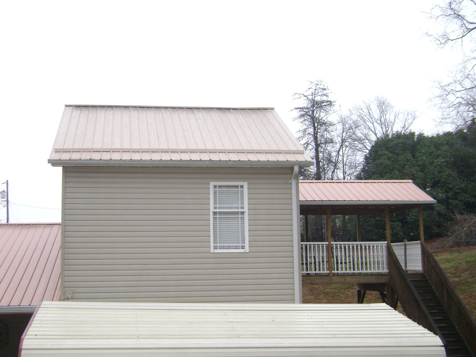 Tan metal roofs on a two story addition and attached porch, from a Roof Replacement job in Iuka